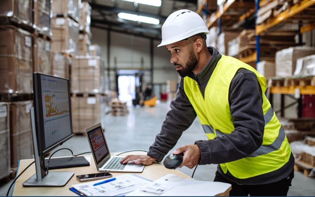 Warehouse worker with multiple computers completing time-consuming, manual tasks for shipping