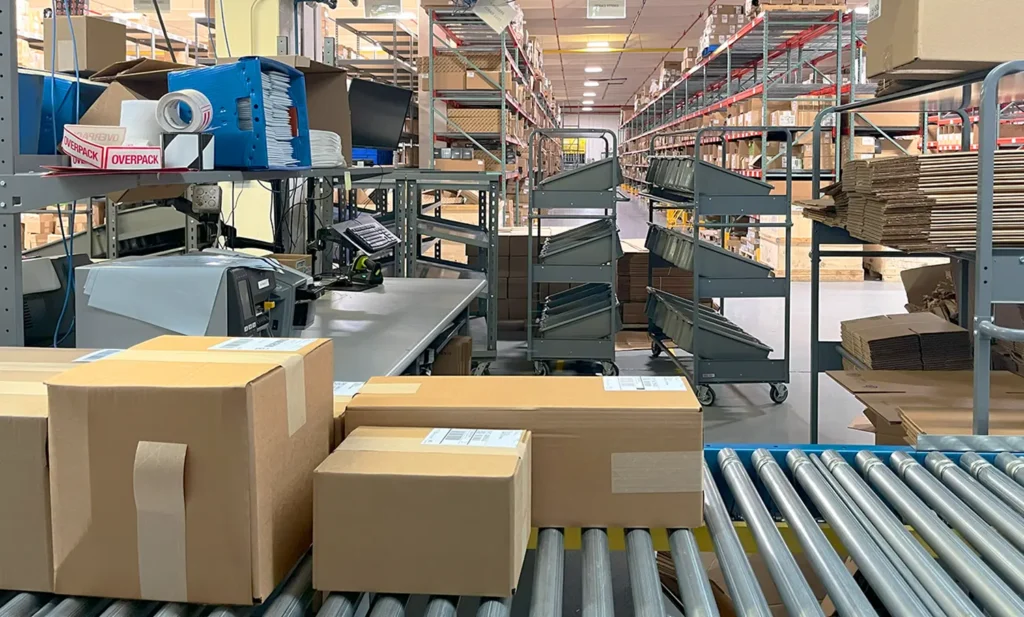 large warehouse shipping station with parcels, label printers, warehouse shipping software, trolleys, and packing supplies.