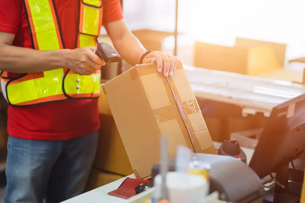 a warehouse worker scanning a parcel with a hand-held barcode scanner connected to warehouse shipping software.