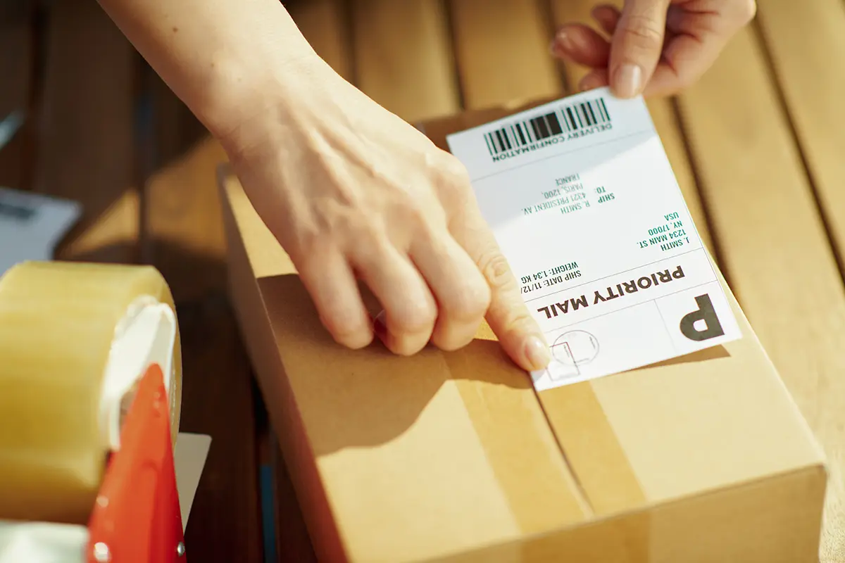 A warehouse worker created a shipping label using shipping management software and is placing the label on a parcel.