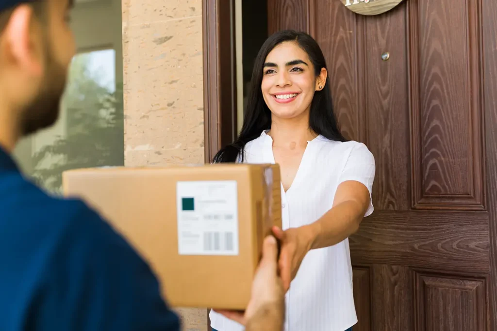 Alt text: A delivery person providing the best ecommerce shipping services to exceed customer expectations as a happy customer receives her parcel at her home .