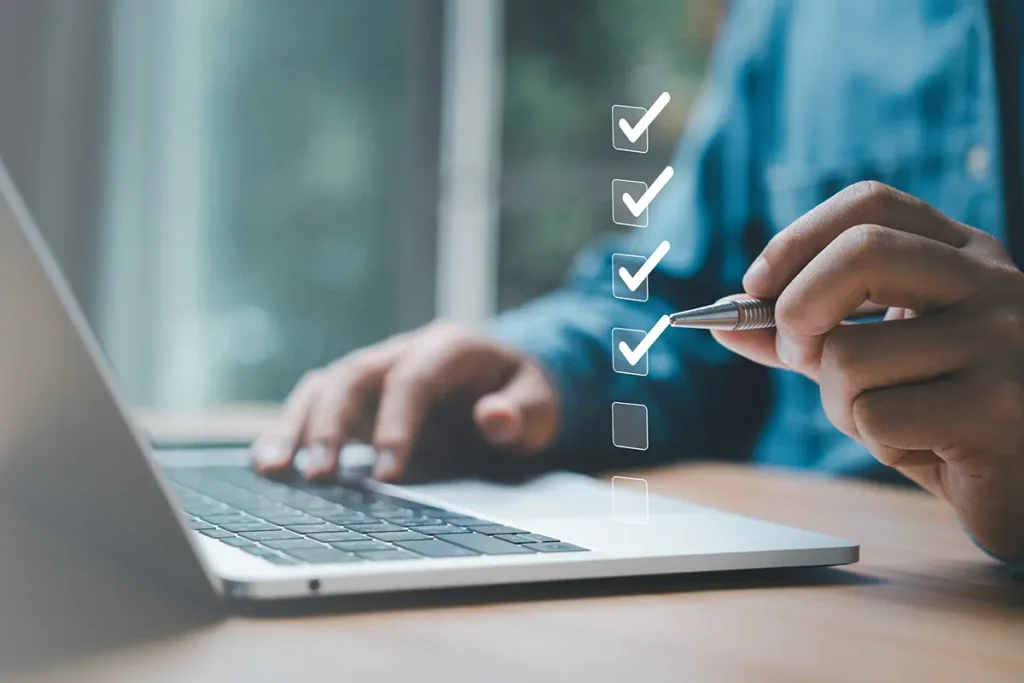 Person using a laptop and a checklist to set up business automation rules to select the best shipping services for ecommerce orders using shipping software.