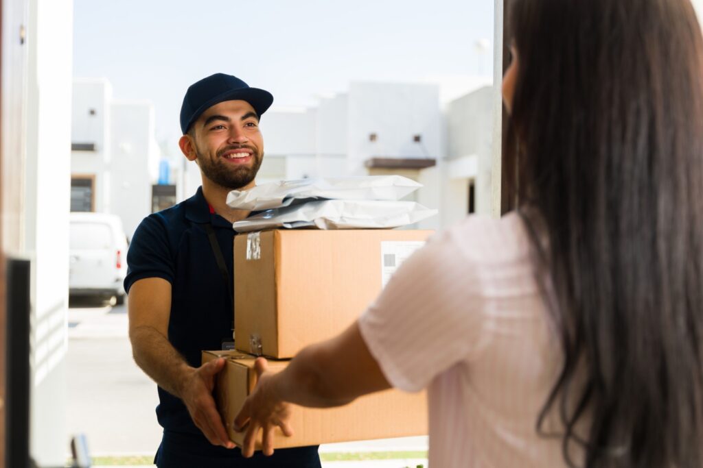 Delivery person from a reliable shipping service handing a stack of ecommerce packages to a happy customer during home delivery.