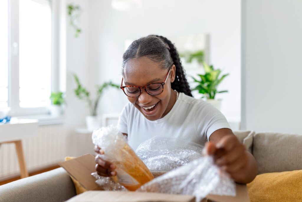 Happy customer is smiling while opening a package because the ecommerce shipping services and product exceeded her expectations. 