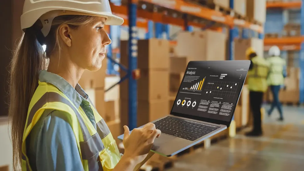 Female warehouse worker using a laptop with warehouse metrics to improve inventory visibility and prevent overselling in ecommerce store