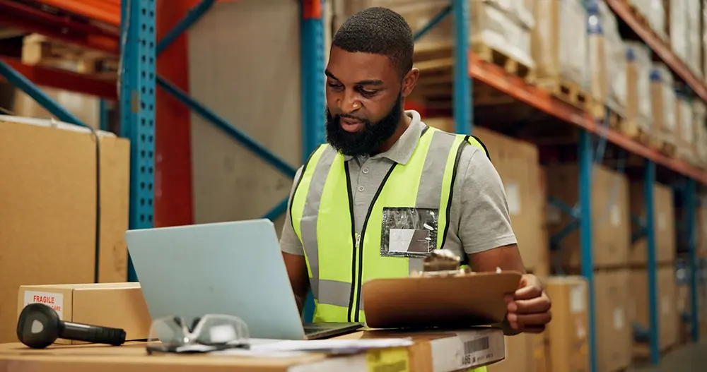 Warehouse Worker Using Manual Shipping and Fulfillment Process with Clipboard and Laptop