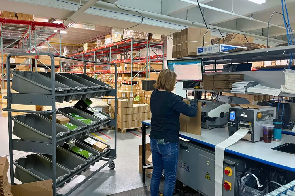 Warehouse worker creating shipping labels for multiple sales channels using shipping software and a thermal label printer