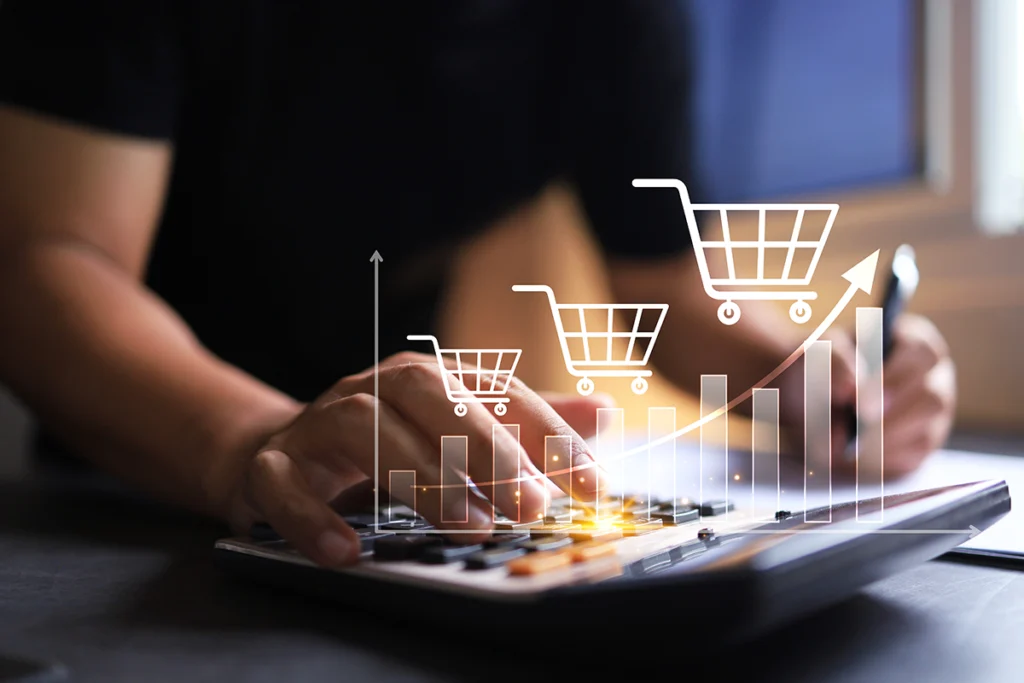An ecommerce business leader uses a calculator overlaid with bar graph and shopping cart graphics with a rising trend line representing an increase in online sales.