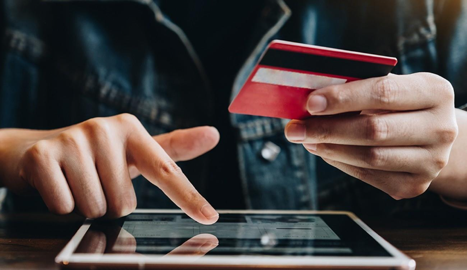 An multichannel ecommerce shopper holding a credit card uses a tablet to make an online purchase.